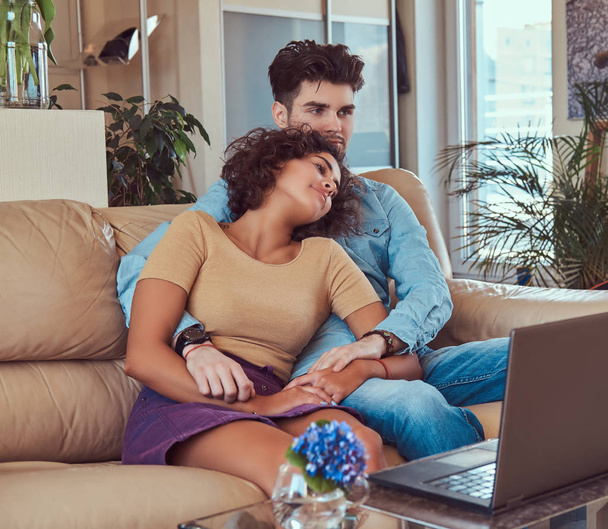 Boldog vonzó pár, egy hétvégén, néz film a laptop otthon a kanapén ül. - Fotó, kép
