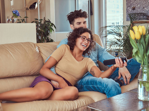 Νεαρό ζευγάρι αγκαλιά ενώ παρακολουθείτε τηλεόραση στο σπίτι. - Φωτογραφία, εικόνα