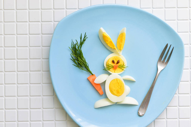 A childrens cheerful breakfast for the kid. rabbit from eggs and carrots. lies on a blue plate - Photo, image