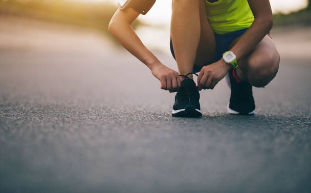 sportswoman tying shoelace before running on city street - Photo, Image