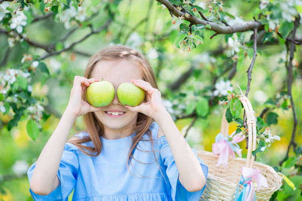 Schattig klein meisje in bloeiende appeltuin op mooie lentedag - Foto, afbeelding