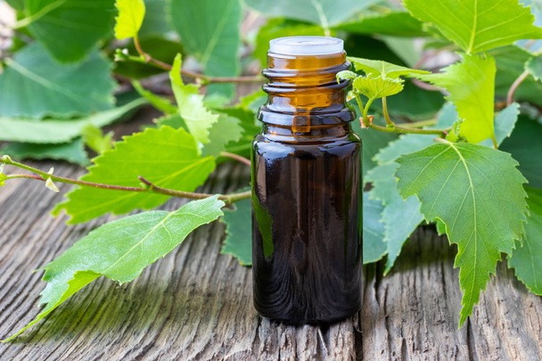 Бутылка эфирного масла с березовыми ветвями на деревянном фоне
 - Фото, изображение
