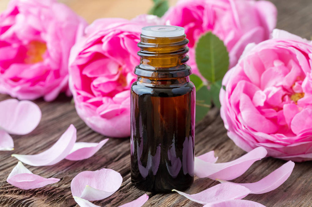 Uma garrafa de óleo essencial com rosas em um fundo de madeira
 - Foto, Imagem