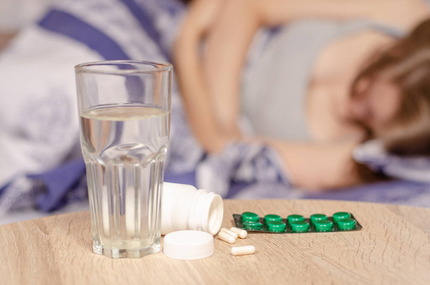 Woman lies in bed sick jar of pills glass of water - Foto, imagen