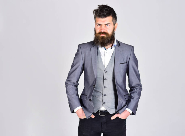 bearded man in business suit on grey background, copy space. hipster in jacket has confindent look. beard care and barber. businessman holds hands in pocket. man with long beard. bearded man in jacket - Фото, зображення