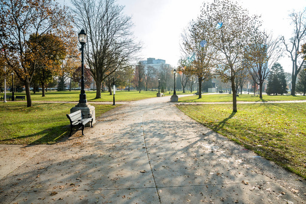 Chemin déserté bordé de bancs et de lampadaires dans un parc municipal par un matin ensoleillé d'automne. London, ON, Canada
. - Photo, image