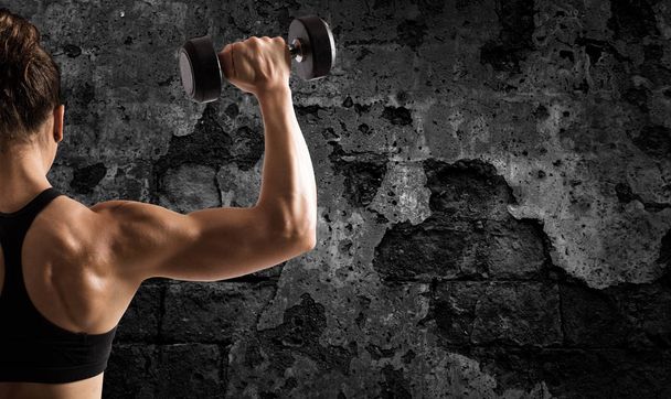 Athletic woman training biceps on grunge background - Photo, Image