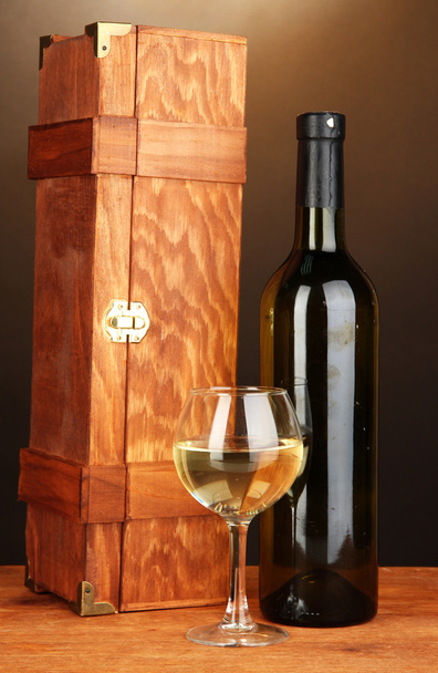 Wooden case with wine bottle on wooden table on brown background - Foto, Bild
