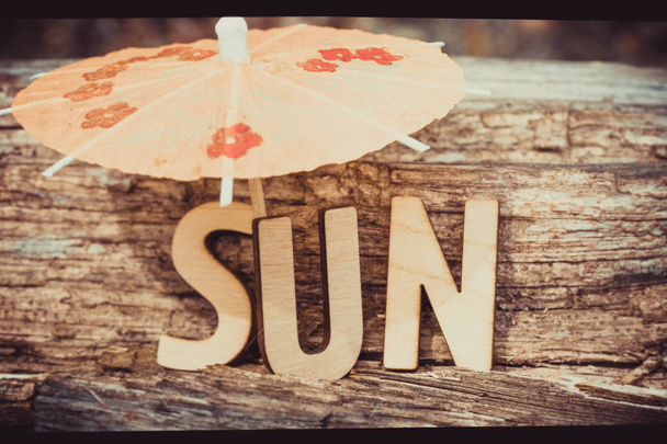 Word Sun is made of wooden letters on old wood background with cocktail umbrella. Tourism, rest, resort, sea, sun, beach concept idea - 写真・画像