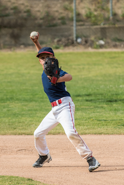 Little League-ben rövid megálló baseball játékos, kar betöltve és készen áll, hogy dobja a labdát át a gyémánt. - Fotó, kép