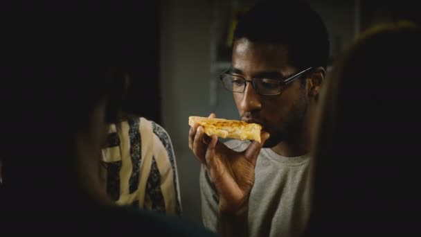 African American young man eating pizza at a casual house party. Young people enjoy fast food in the kitchen at home. - Záběry, video