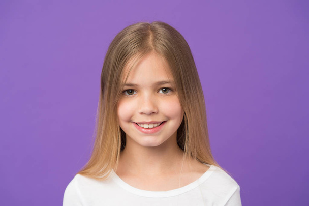 Beauty look and skincare. Little girl smile on violet background. Child with fresh skin on cute face. Beauty kid with happy look and long blond hair on purple background. Childhood and childcare - Φωτογραφία, εικόνα
