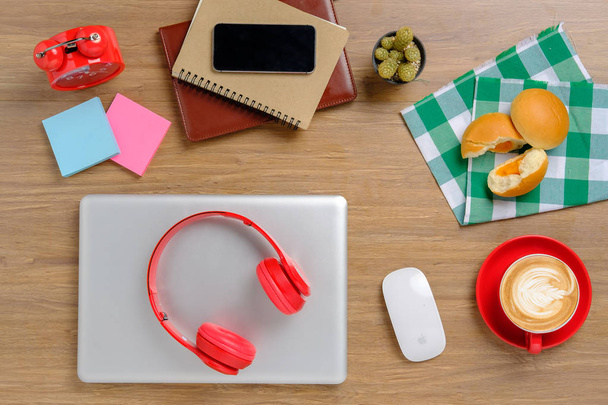 Γραφείο τραπέζι με laptop, αρτοποιείο, notebook, smartphone, ακουστικά και φλιτζάνι καφέ. - Φωτογραφία, εικόνα