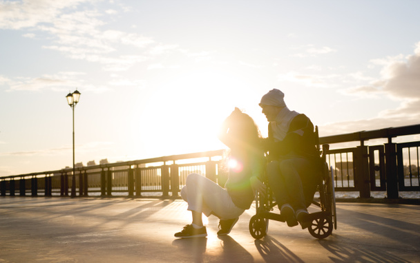 Couple heureux - jeune femme avec un homme handicapé en fauteuil roulant repose ensemble à l'extérieur
 - Photo, image
