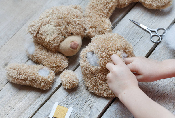A girl sews a bear toy. Handicraft with children. Child fills the toy with a sintepon. - Fotó, kép