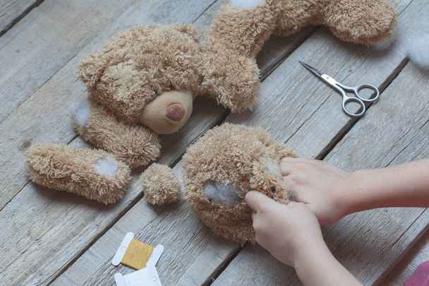 A girl sews a bear toy. Handicraft with children. Child fills the toy with a sintepon. - Photo, Image