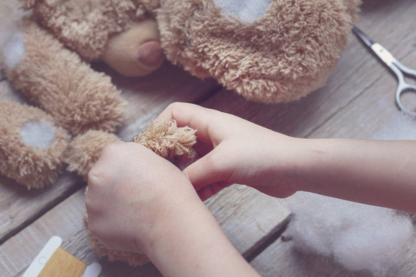 Una chica cose un juguete de oso. Artesanía con niños. El niño llena el juguete con un sintepón. Tonificación
 - Foto, imagen