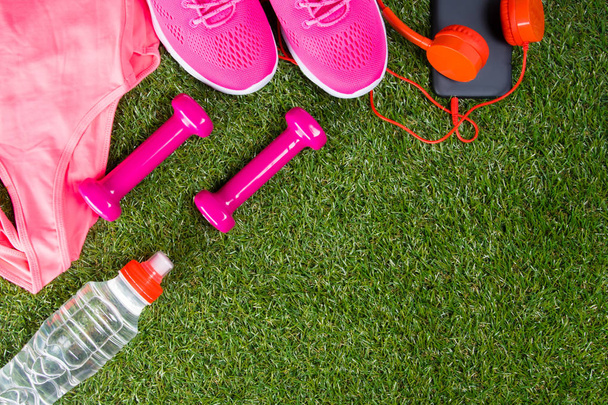 pink sportswear and accessories for fitness, and a bottle of water, in the background of grass with a place for writing - Foto, Imagem