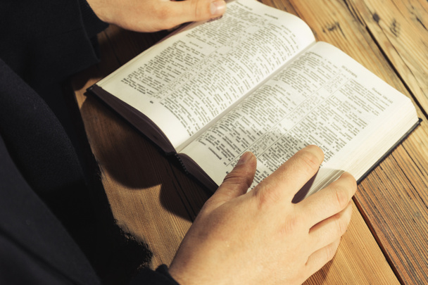 Hombre sentado en una vieja mesa de roble leyendo la Sagrada Biblia
 - Foto, Imagen