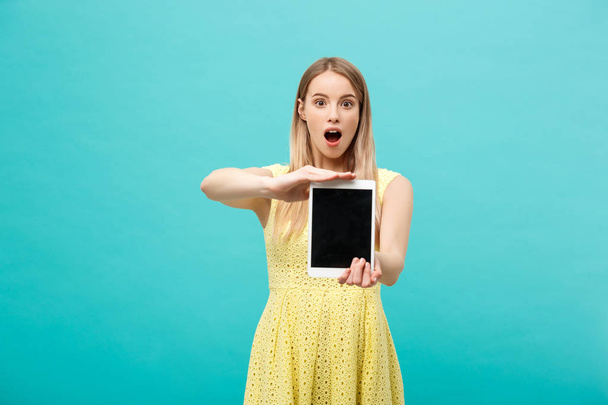 Excited shocked good-looking young woman in yellow dress having confused or puzzled expression on face while receiving urgent message or email, using wi-fi on tablet. - Fotó, kép