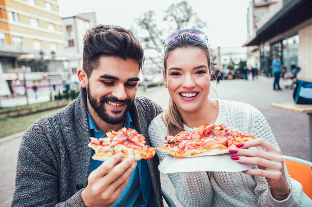 屋外でピザを食べ、笑顔を見せるカップル屋外カフェでピザをシェアしています. - 写真・画像