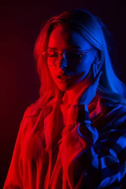 Nahaufnahme Porträt einer attraktiven jungen Frau mit Brille und gestreifter Bluse, die mit rotem und blauem Licht im Gesicht posiert - Foto, Bild