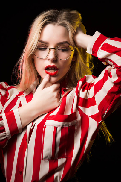 Closeup portrait of fabulous blonde girl with red lips, wearing glasses, posing with red and yellow light at studio - Фото, изображение