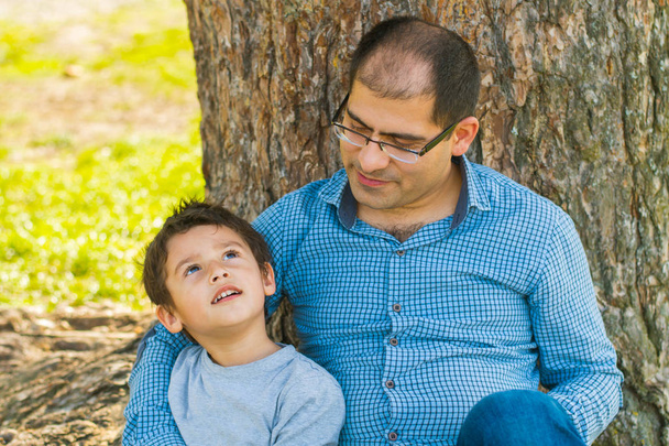 父と息子は、夏に大きな木の下に座ってください。 - 写真・画像