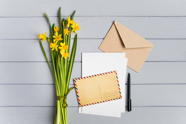 Letter, postcard, envelope and daffodils bouquet on grey wooden background. Wedding invitation cards or love letter. Romantic holiday concept, top view, flat lay, overhead view - Fotoğraf, Görsel