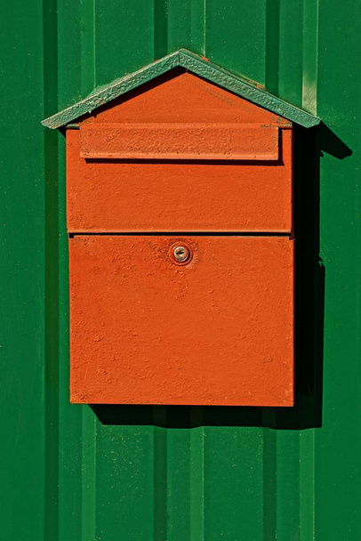 помаранчева поштова скринька на зеленій металевій стіні
 - Фото, зображення