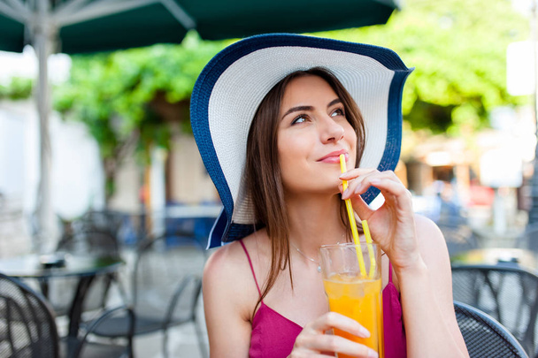 Mujer en la terraza de la calle en pueblo griego en un caluroso día de verano bebiendo un zumo de naranja. Verano ambiente mediterráneo, viajes y concepto de ocio
. - Foto, Imagen