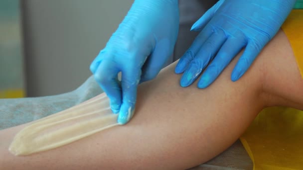Close-up of the hand in rubber gloves is applied to the hair removal paste and by special technology shugaring removes hair - Footage, Video