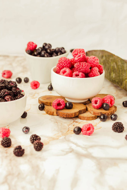 Raw raspberries and blueberries in white cups. white marble background. Summer fruit, berries. Space for text. Detox diets and healthy food concept. - Foto, Imagem