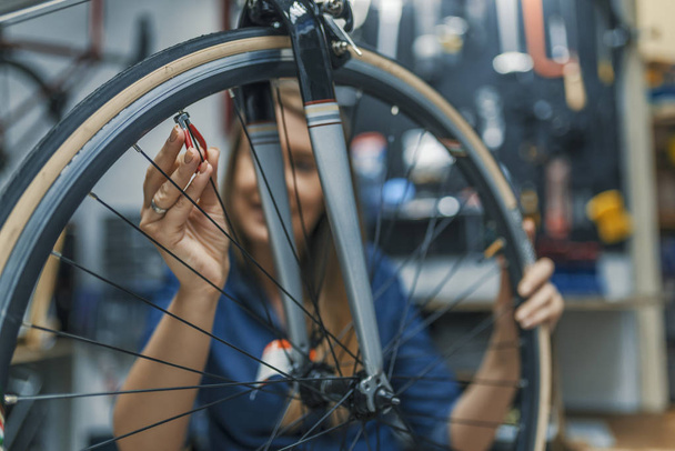 Mechanic repairing gears of bicycle. Repair and tuning, adjustment, disc brake on a bicycle. Stylish bicycle mechanic woman doing his professional work in workshop. - Photo, Image