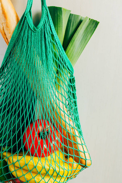 Green string shopping bag with vegetables, fruits and bread hanging on a hook in the kitchen. Close up. - Photo, Image