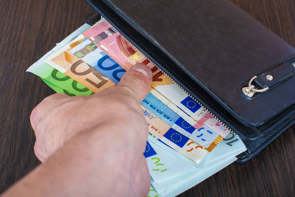 La main de l'homme tire des billets avec un sac à main en cuir et le retrait de la monnaie européenne euro, euro
  - Photo, image
