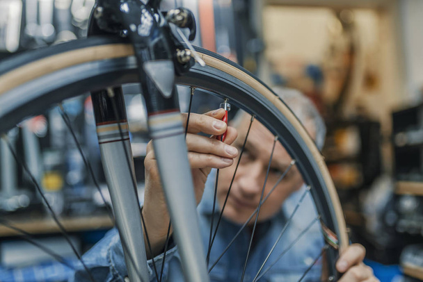 Service for bike with adept repairing bike. Bicycle mechanic in a workshop in the repair process. Stylish bicycle mechanic doing his professional work in workshop.  - Фото, зображення
