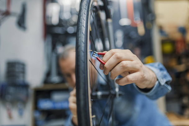 Service for bike with adept repairing bike. Bicycle mechanic in a workshop in the repair process. Stylish bicycle mechanic doing his professional work in workshop.  - 写真・画像