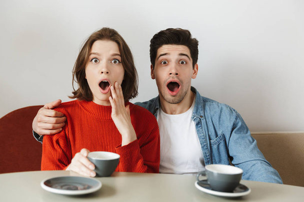 Caucasian woman and man expressing surprise with open mouth while drinking coffee or tea in cafe - Fotó, kép