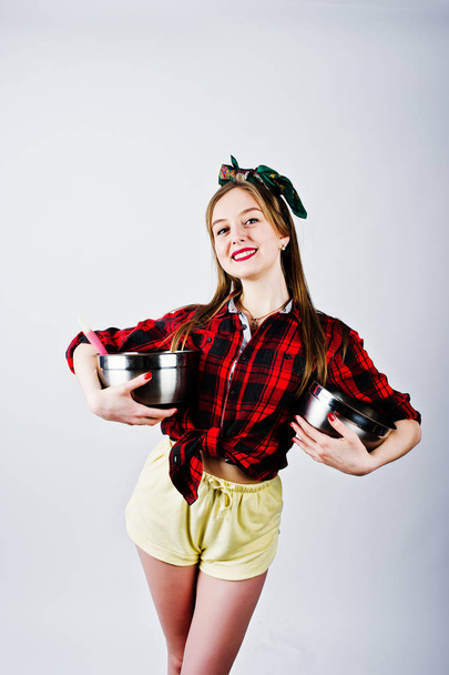 Young funny housewife in checkered shirt and yellow shorts pin up style with two saucepan isolated on white background. - Foto, Bild