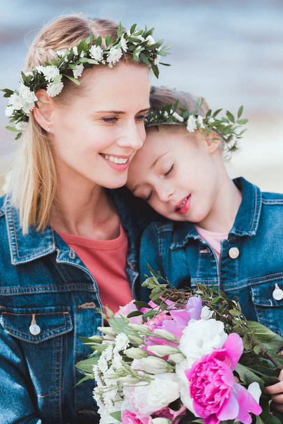 красивые улыбающиеся мать и дочь с закрытыми глазами в цветочных венках
  - Фото, изображение