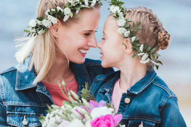 happy mother and daughter in floral wreaths touching noses - Photo, Image