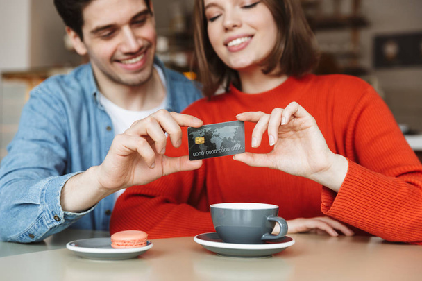 Blurry image of beautiful happy couple man and woman sitting at table in cafe and holding credit card together - Foto, imagen