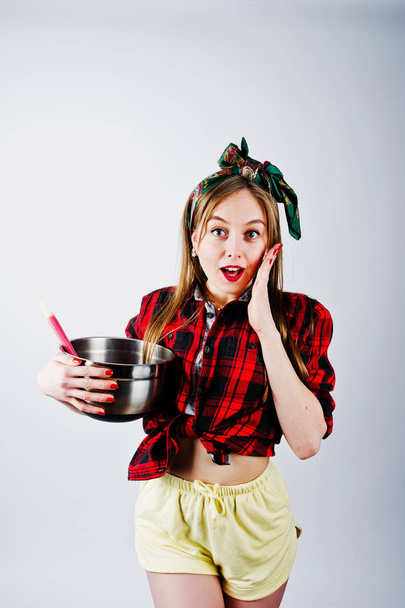 Young funny housewife in checkered shirt and yellow shorts pin up style with saucepan and kitchen spoon isolated on white background. - Valokuva, kuva