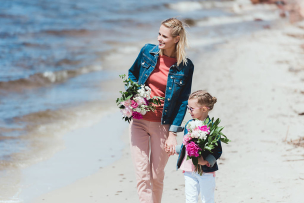 привлекательная мать и дочь с букетами, держащимися за руки на берегу моря
 - Фото, изображение