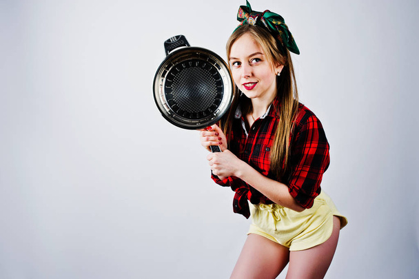 Young funny housewife in checkered shirt and yellow shorts pin up style with frying pan isolated on white background. - Photo, image