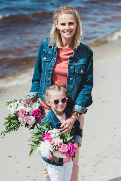 mother and daughter with peony bouquets on sea shore - Photo, Image