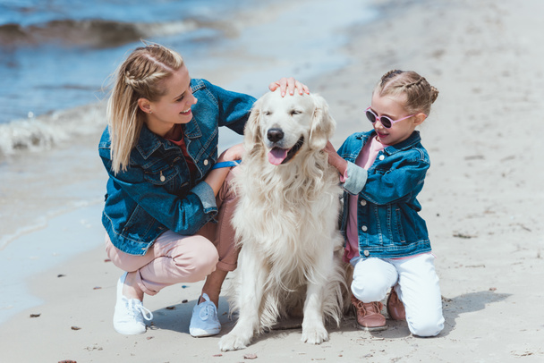happy family sitting with golden retriever dog on sea shore - Photo, Image