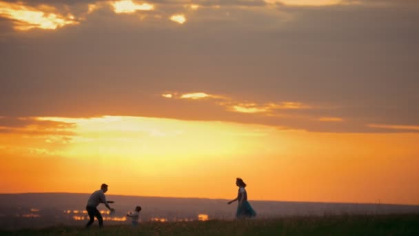 Fiatal nő, és az ő férje, játék frisbee, a mező, mellette kis fiuk, naplemente, nyári este - Felvétel, videó