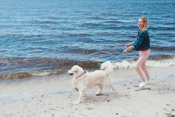 attractive happy woman walking with dog on sea shore - Foto, afbeelding